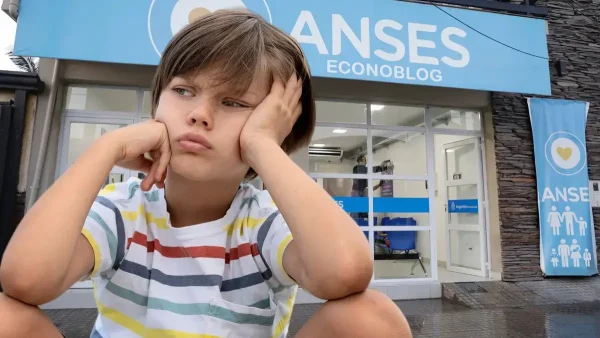 Niño triste en oficina de Anses con cartel de AUH y SUAF