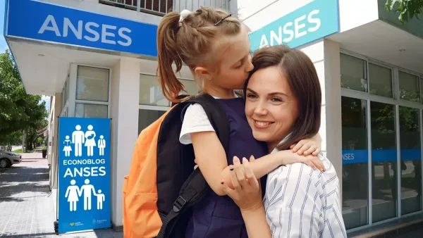 Estudiante con su madre en Anses con cartel de AUH y SUAF