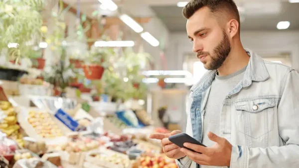 Joven con su celular comprando en un supermercado