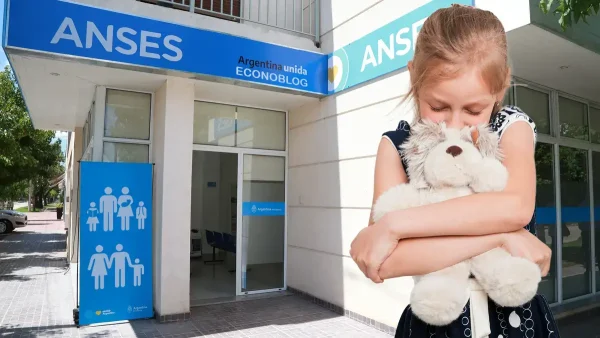 Niña triste abrazada a su oso con cartel de Anses para AUH y SUAF