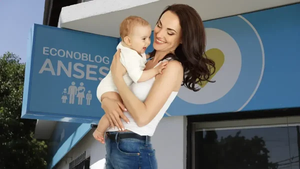 Madre de la AUH feliz frente a cartel de Anses