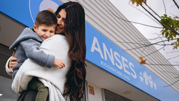 Madre abrazada a su hijo en Anses con cartel de AUH